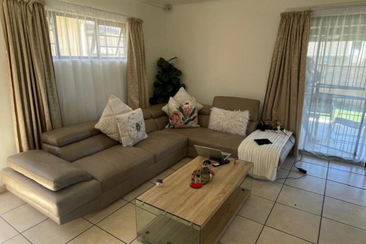 A living room featuring ceramic floor tiles, large windows, and a sliding glass door providing access to the outdoor patio area.