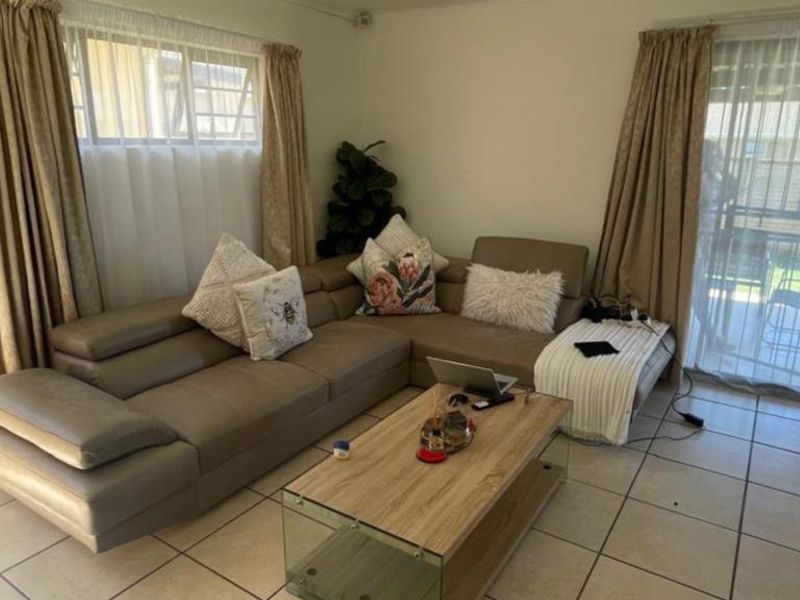 A living room featuring ceramic floor tiles, large windows, and a sliding glass door providing access to the outdoor patio area.