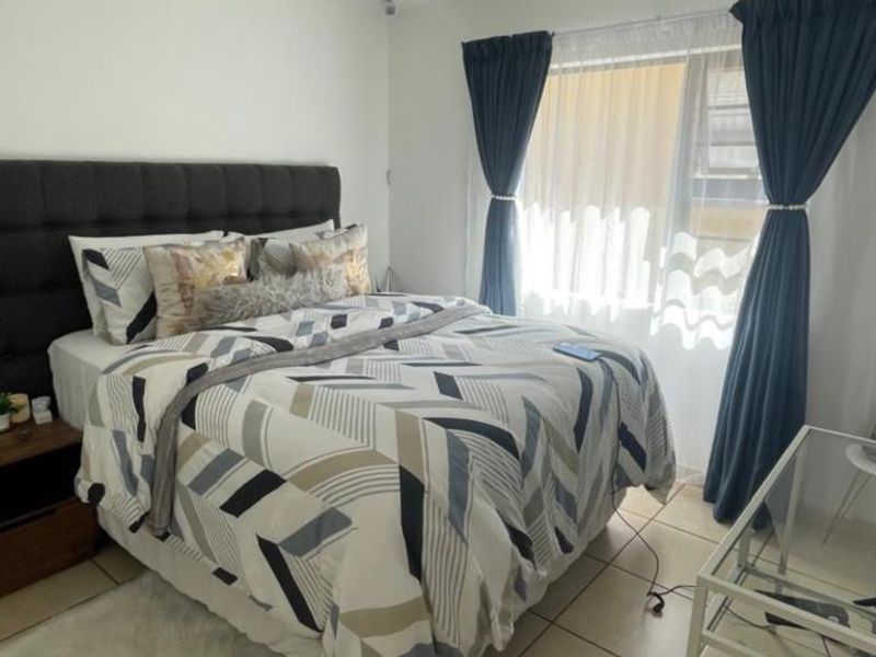 A functional bedroom featuring tiled flooring and large windows with curtain rails, providing natural light and a comfortable living space.