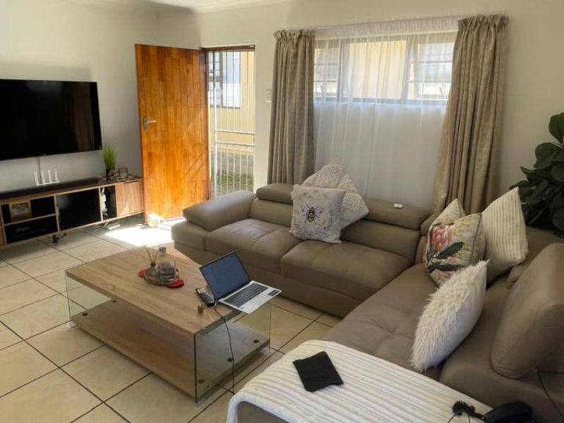 A comfortable living room featuring tiled flooring, a wooden entrance door, and large windows with curtains, providing a bright and functional living space.