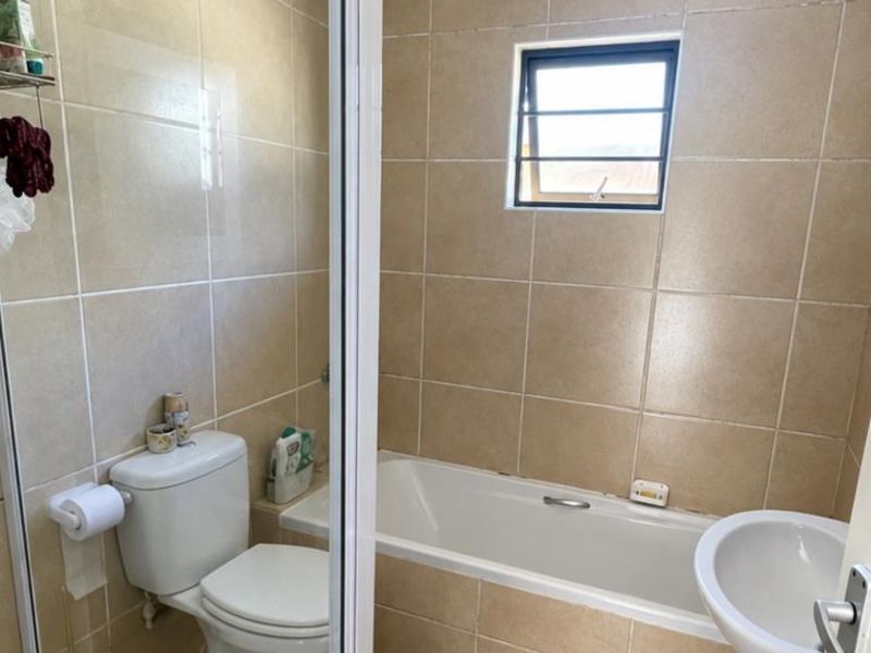 A functional bathroom featuring a bathtub, toilet, and washbasin with neutral wall tiling and a louvered window for ventilation.