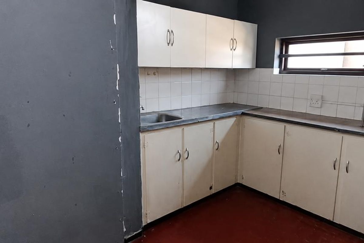 A compact, empty kitchen featuring built-in cabinetry, a stainless steel sink, and tiled backsplash, currently requiring cosmetic updates and wall repairs.