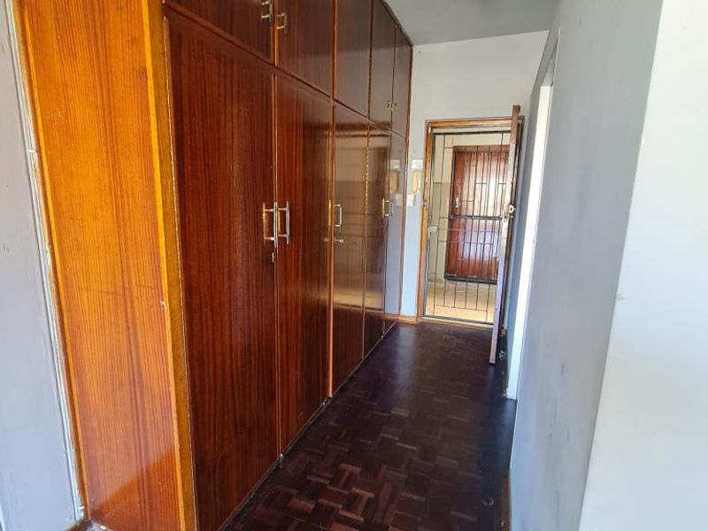 A hallway featuring extensive built-in wooden cabinetry and traditional parquet flooring, leading towards a secure entrance door.