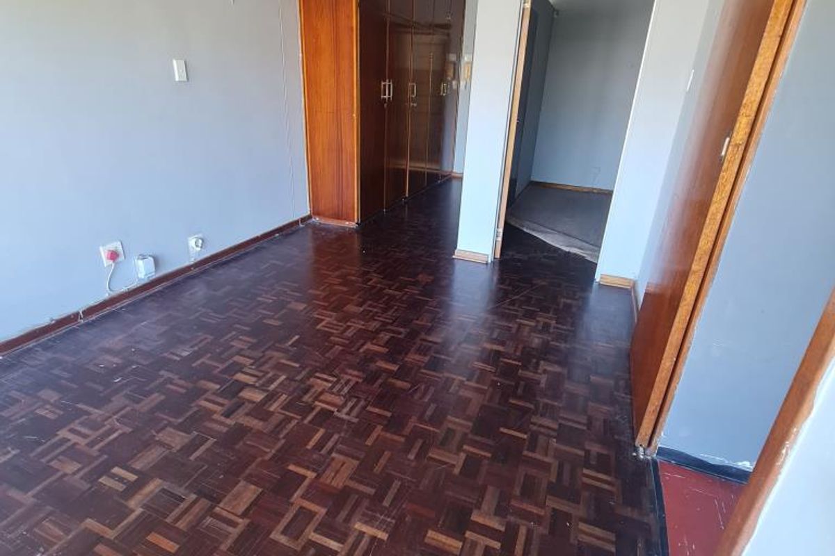 An empty bedroom featuring original parquet flooring and built-in wooden cupboards, offering a blank canvas for renovation and modernization.