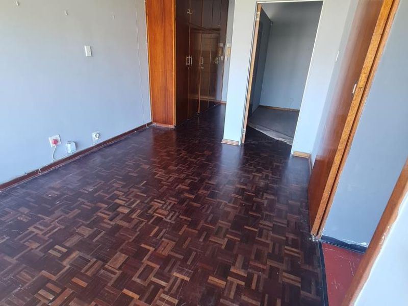 An empty bedroom featuring original parquet flooring and built-in wooden cupboards, offering a blank canvas for renovation and modernization.