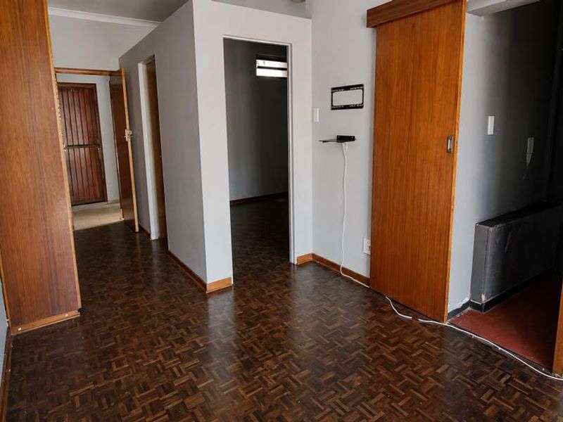 A vacant hallway featuring traditional parquet flooring, wooden door frames, and sliding doors, providing access to multiple rooms within the apartment.