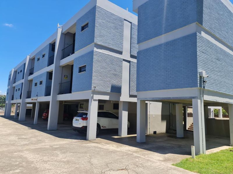 Exterior view of a multi-story apartment complex featuring painted brick facades, concrete support pillars, and covered ground-level parking bays.