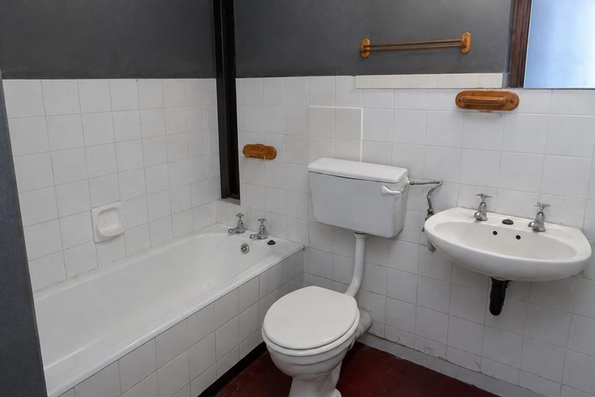A functional bathroom featuring a standard bathtub, pedestal basin, and toilet with white wall tiling and dark painted upper walls.