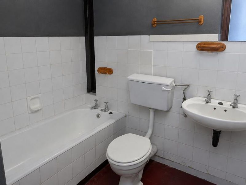 A functional bathroom featuring a standard bathtub, pedestal basin, and toilet with white wall tiling and dark painted upper walls.