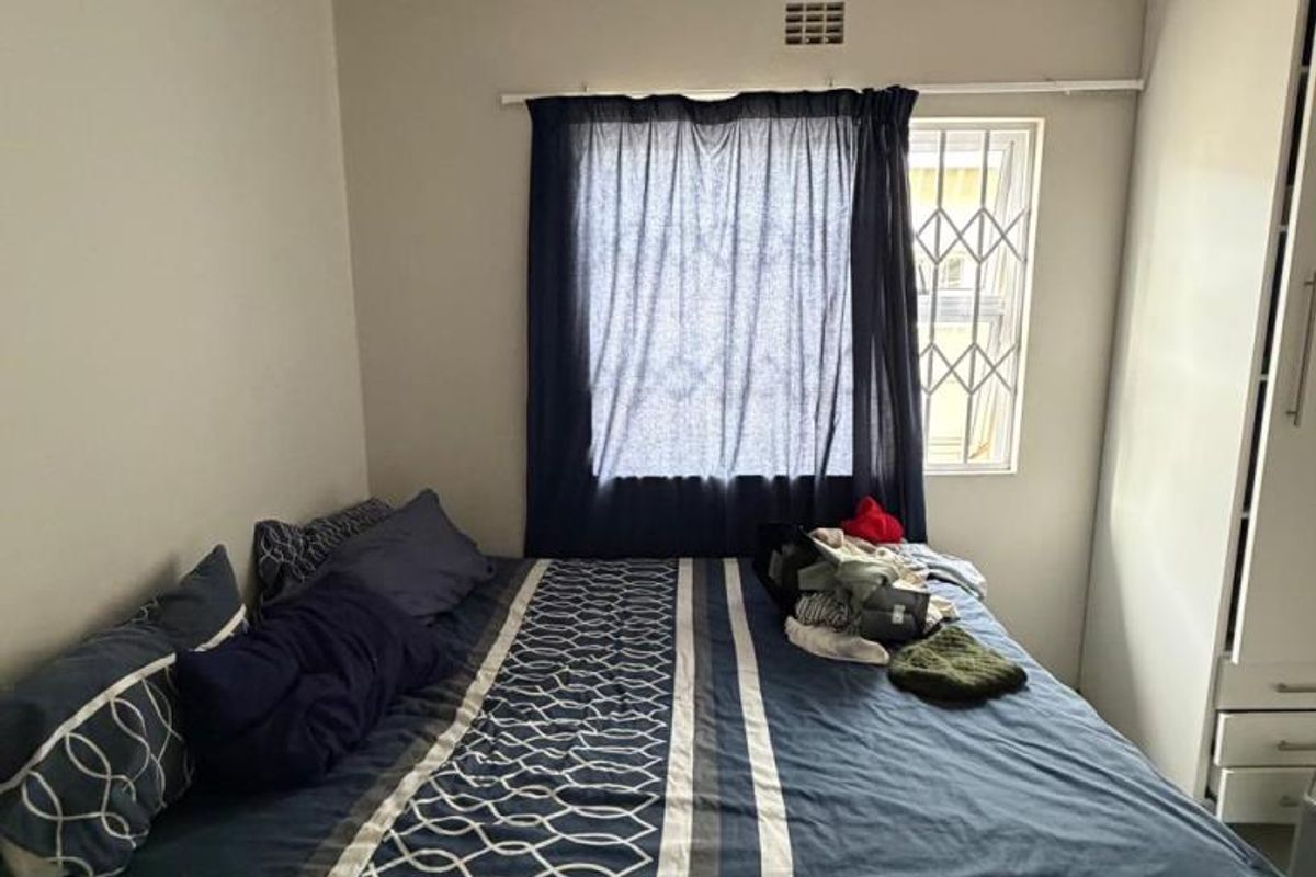 A functional bedroom featuring a built-in wardrobe, security bars on the window, and a timber panel ceiling.