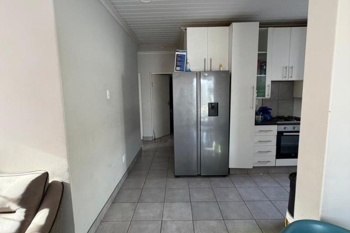 A functional kitchen area featuring tiled flooring, white cabinetry, and a tongue and groove ceiling, leading into a secondary hallway space.