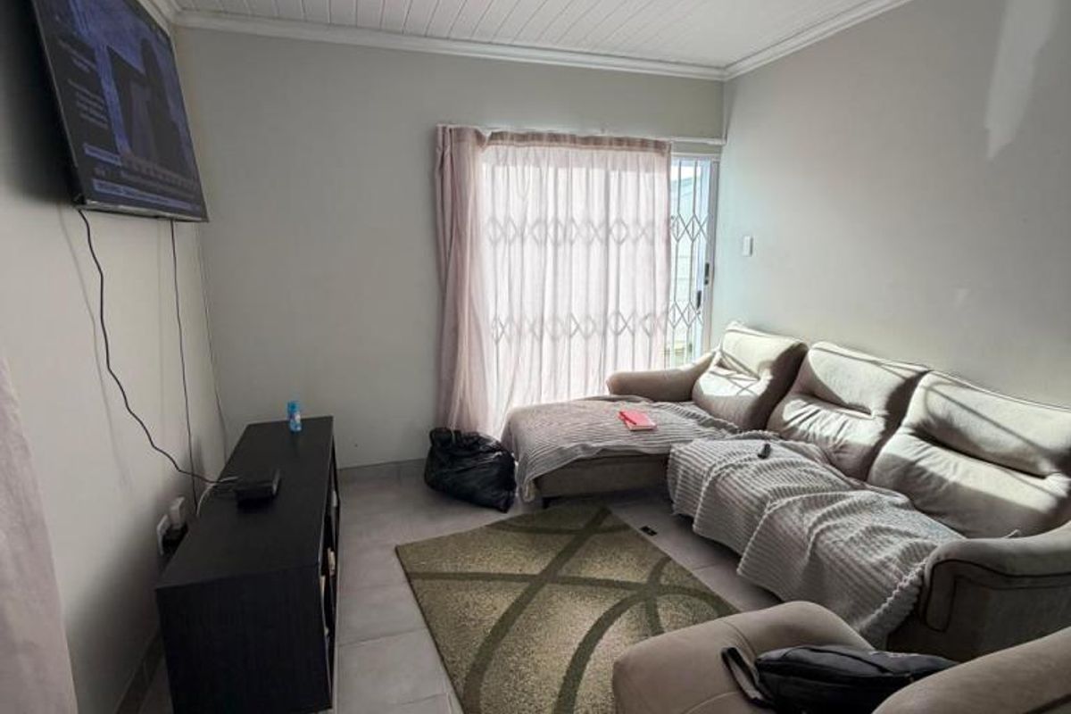 A living room featuring tiled flooring, a tongue and groove ceiling, and a sliding glass door with a security gate leading outdoors.
