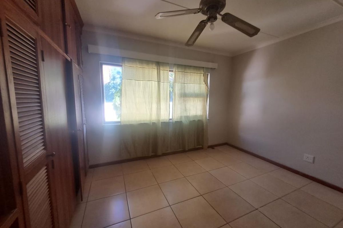 A spacious, empty bedroom featuring tiled flooring, a ceiling fan, and extensive built-in wooden cabinetry for storage.