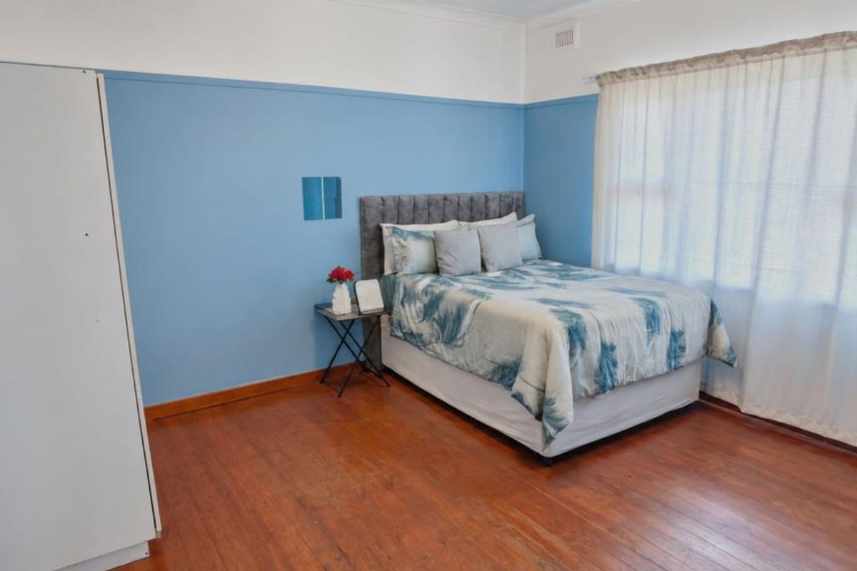 A bedroom featuring original timber flooring, blue wall panelling, and large windows with curtains, offering a classic aesthetic ready for a modern update.