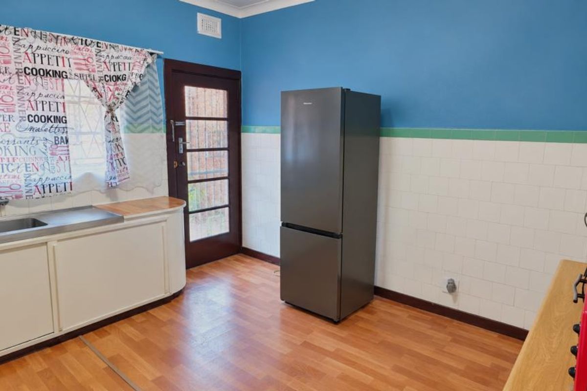 A functional kitchen featuring built-in cabinetry, a stainless steel sink, tiled splashbacks, and direct access to the exterior via a glass-paneled door.