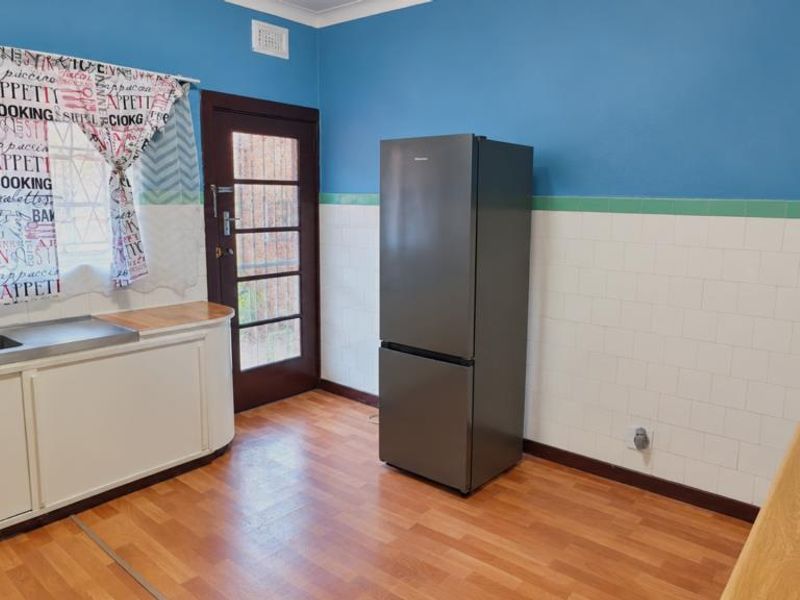 A functional kitchen featuring built-in cabinetry, a stainless steel sink, tiled splashbacks, and direct access to the exterior via a glass-paneled door.