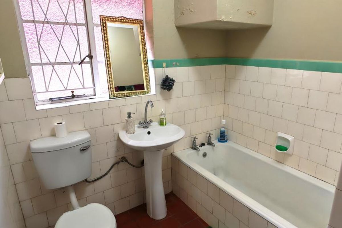 A dated bathroom featuring a pedestal basin, bathtub, and tiled walls. The space requires cosmetic updates to improve its overall condition and appeal.