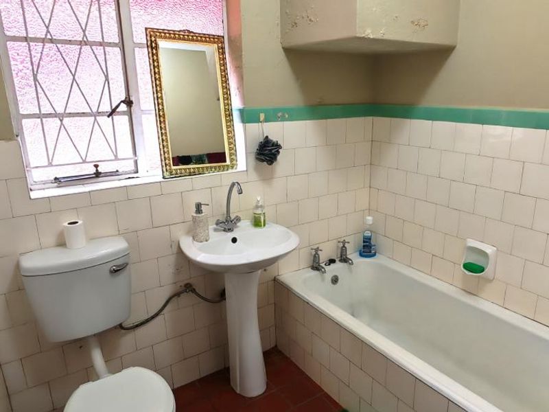 A dated bathroom featuring a pedestal basin, bathtub, and tiled walls. The space requires cosmetic updates to improve its overall condition and appeal.