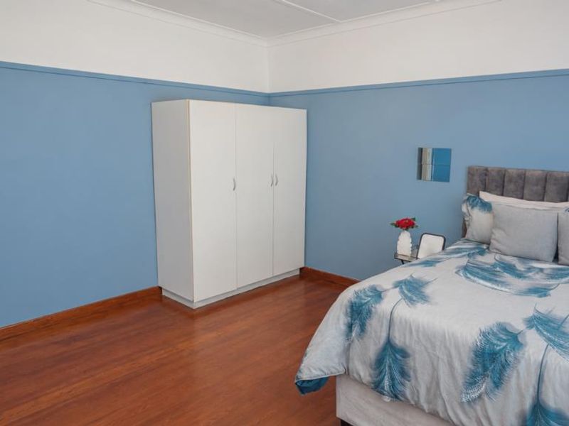 A well-maintained bedroom featuring polished hardwood flooring, a built-in wardrobe, and decorative coving, offering a clean and functional living space.