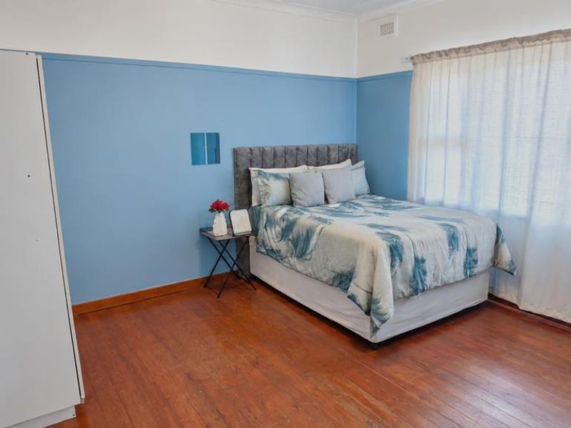 A bedroom featuring original timber flooring, blue wall panelling, and large windows with curtains, offering a classic aesthetic ready for a modern update.