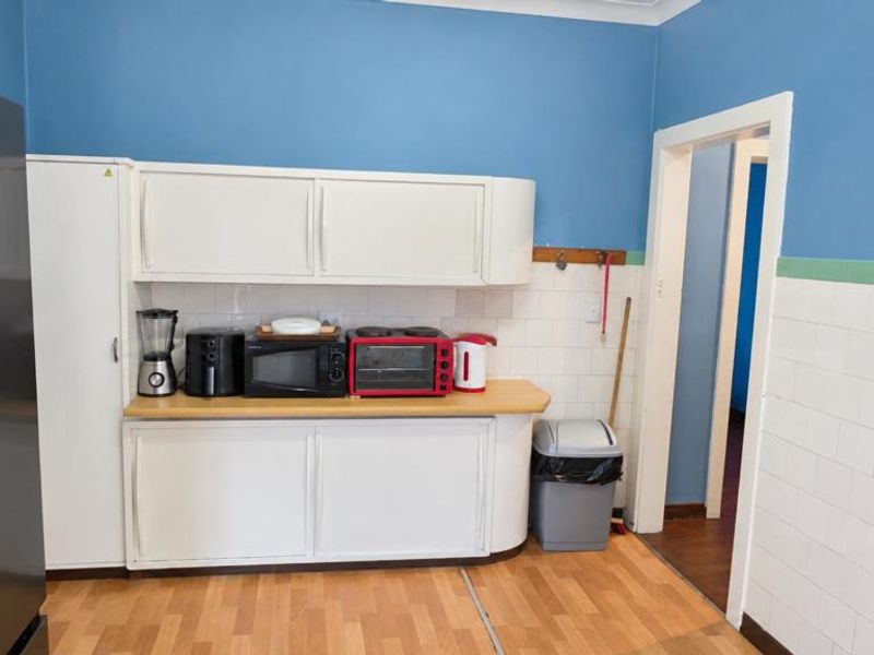 A functional kitchen area featuring white built-in cabinetry, laminate countertops, and a tiled splashback, requiring cosmetic updates to modernize the space.