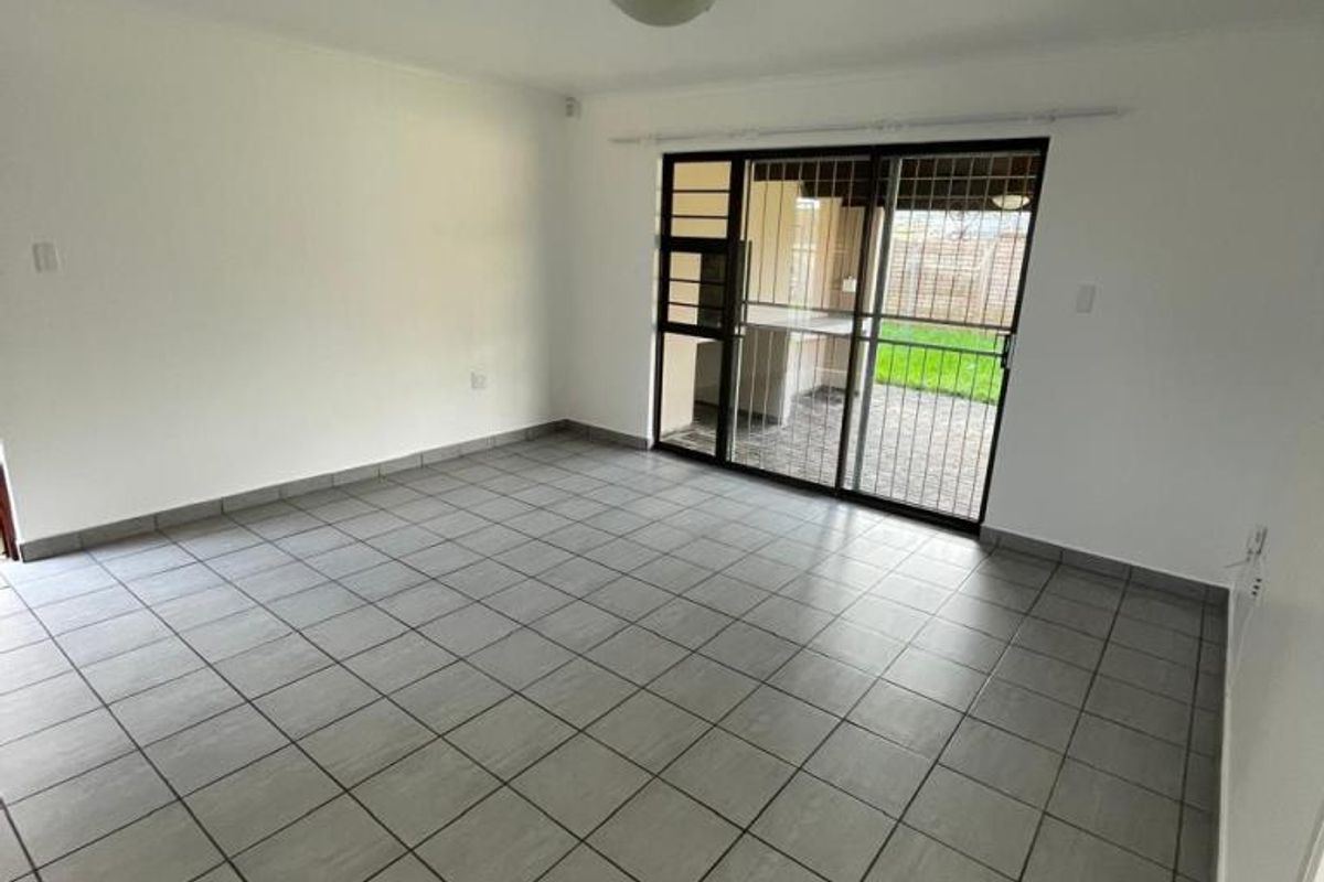 A bright, empty living room featuring neutral tiled flooring and a large sliding glass door with security gate providing access to the outdoor area.