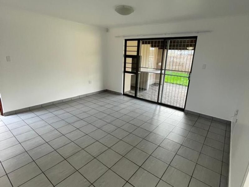 A bright, empty living room featuring neutral tiled flooring and a large sliding glass door with security gate providing access to the outdoor area.