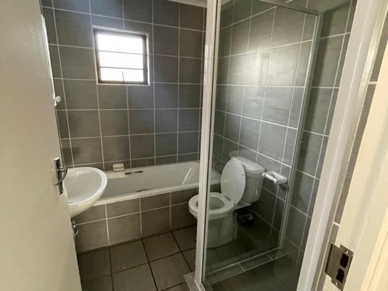 A functional bathroom featuring a bathtub, separate shower enclosure, toilet, and pedestal basin with neutral grey wall and floor tiling.