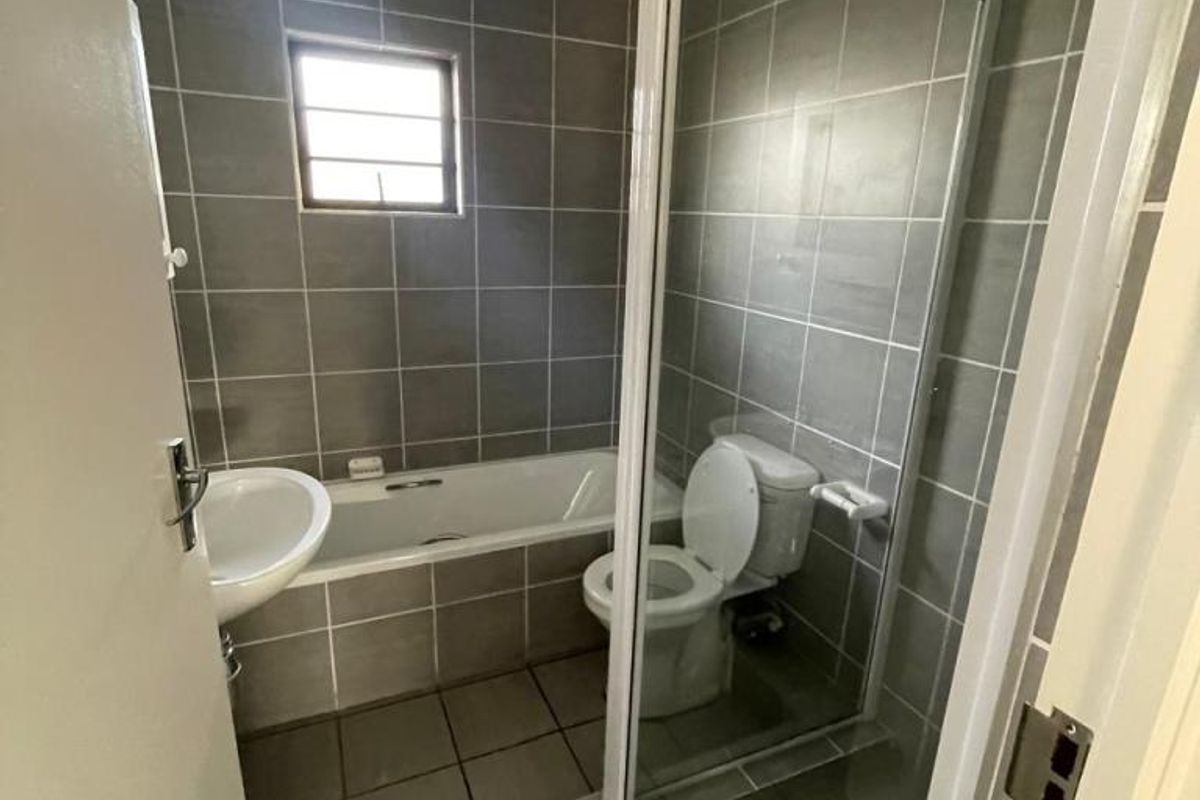 A functional bathroom featuring a bathtub, separate shower enclosure, toilet, and pedestal basin with neutral grey wall and floor tiling.