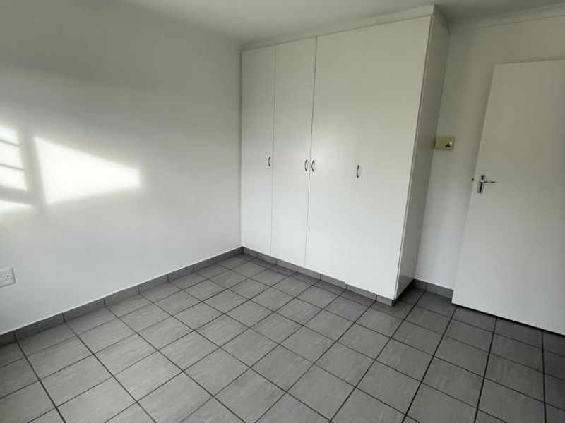 A clean, empty bedroom featuring neutral grey tiled flooring and white built-in cupboards, offering a versatile space ready for personalization.