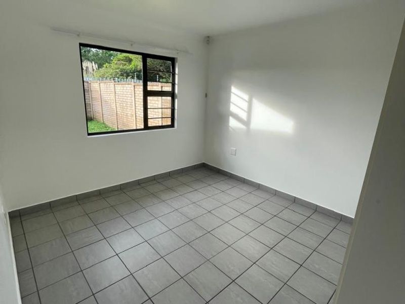 A clean, empty bedroom featuring neutral grey floor tiles, white walls, and a large window providing natural light.