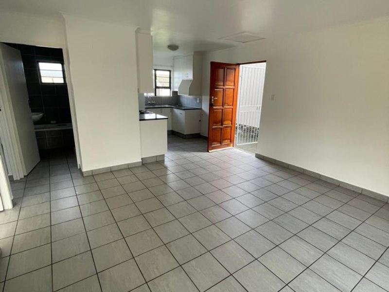 An open-plan living and kitchen area featuring neutral tiled flooring, white cabinetry, and direct access to an exterior space.