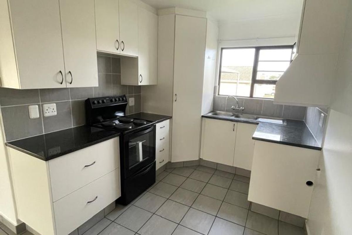 A functional kitchen featuring white cabinetry, dark countertops, a double basin sink, and tiled flooring, offering a clean and practical workspace.