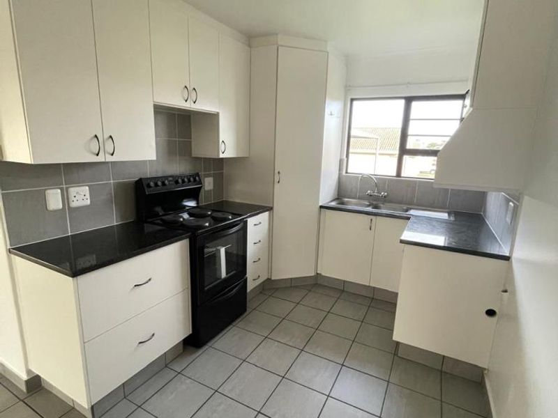 A functional kitchen featuring white cabinetry, dark countertops, a double basin sink, and tiled flooring, offering a clean and practical workspace.