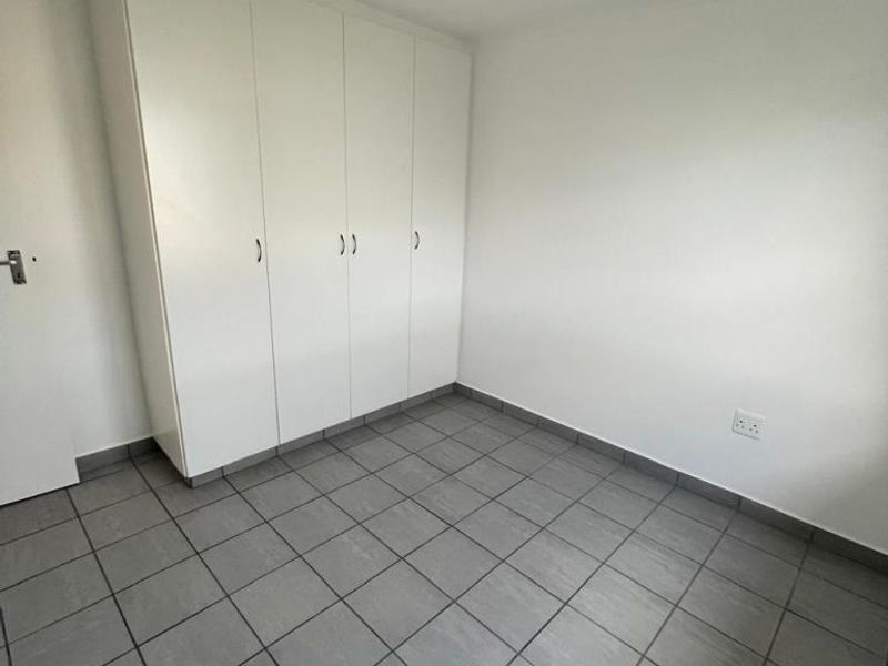 A clean, empty bedroom featuring neutral tiled flooring and ample built-in cupboard storage, providing a versatile space ready for personalization.