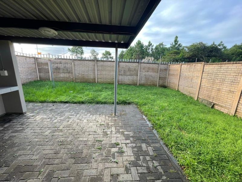A private backyard featuring a covered patio with a built-in braai, brick paving, and a fully enclosed garden with perimeter electric fencing.