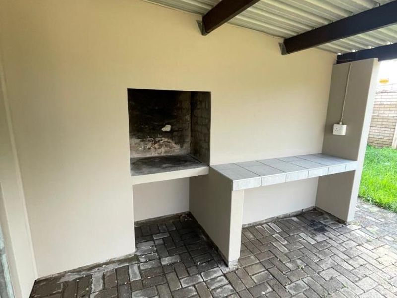 Covered outdoor patio area featuring a built-in braai, tiled prep counter, and durable paved flooring, ideal for outdoor entertaining.