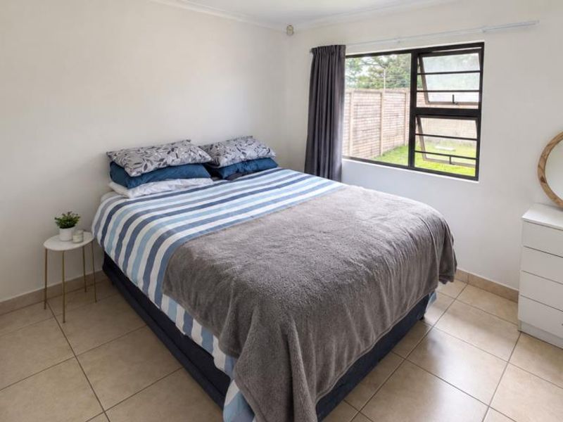 A clean, empty bedroom featuring neutral grey floor tiles, white walls, and a large window providing natural light.