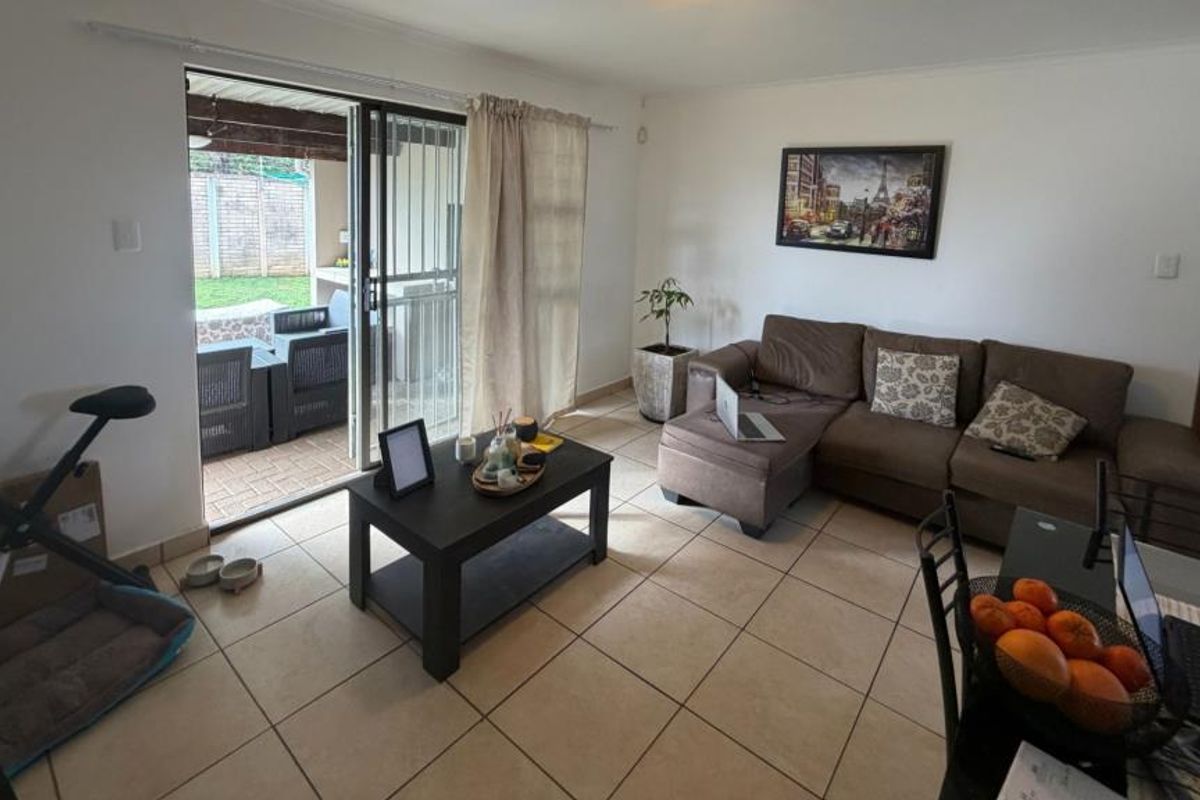 A bright, empty living room featuring neutral tiled flooring and a large sliding glass door with security gate providing access to the outdoor area.
