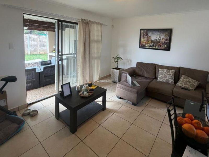 A bright, empty living room featuring neutral tiled flooring and a large sliding glass door with security gate providing access to the outdoor area.