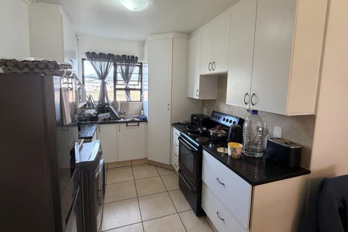 A clean, empty bedroom featuring neutral tiled flooring, a built-in cupboard, and a window fitted with security burglar bars.