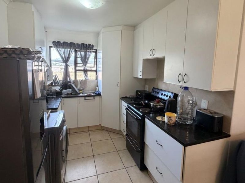 A clean, empty bedroom featuring neutral tiled flooring, a built-in cupboard, and a window fitted with security burglar bars.