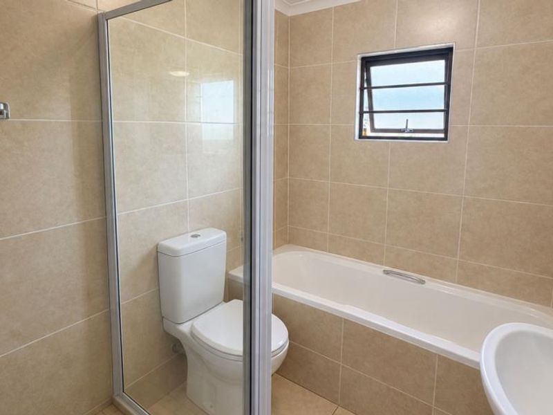 A private backyard featuring a covered patio with a built-in braai, brick paving, and a fully enclosed garden with perimeter electric fencing.