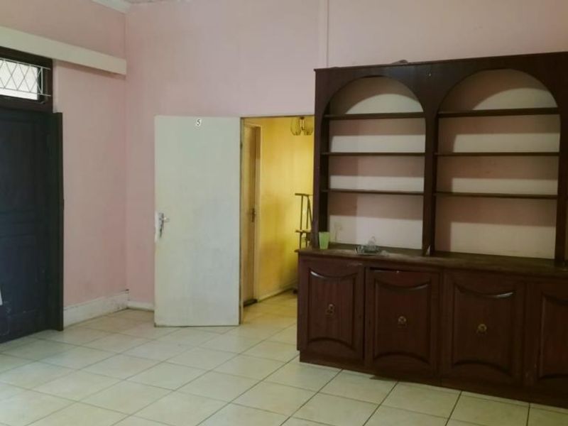Spacious living area featuring tiled flooring, a large built-in timber shelving unit, and direct access to an adjoining room.