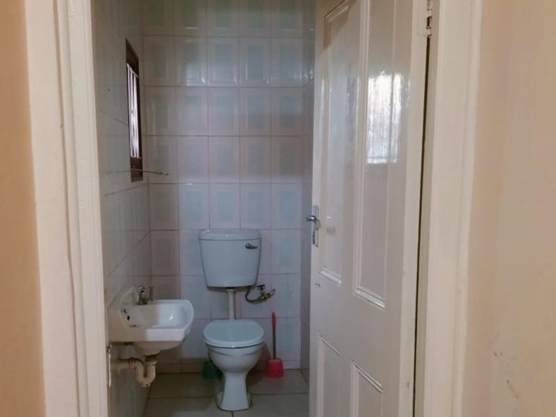 A compact bathroom featuring a wall-mounted basin and toilet with tiled walls and flooring, presenting a dated but functional space.