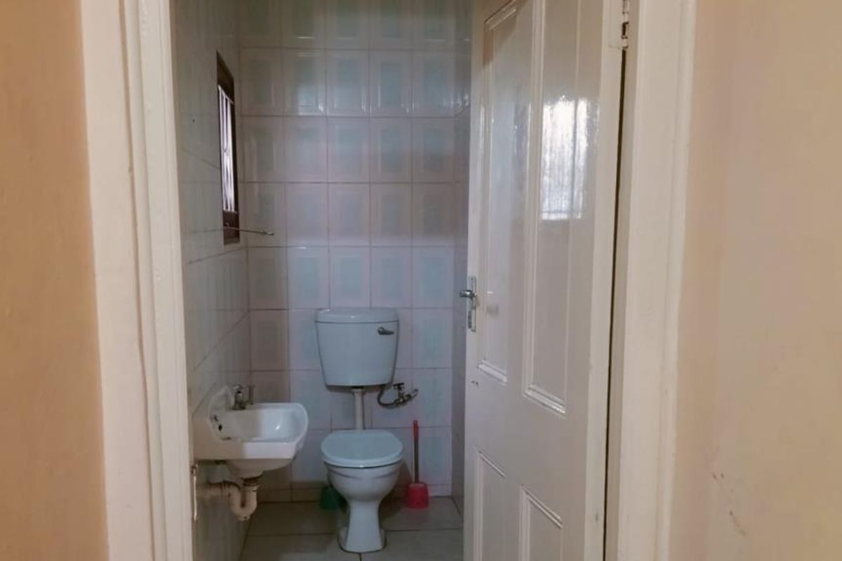 A compact bathroom featuring a wall-mounted basin and toilet with tiled walls and flooring, presenting a dated but functional space.