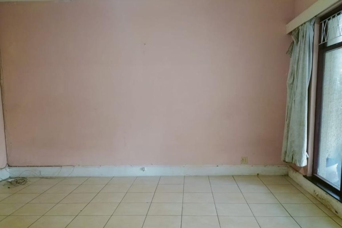 An empty living room featuring tiled flooring and a large window, requiring cosmetic updates and wall repairs to improve its overall condition.