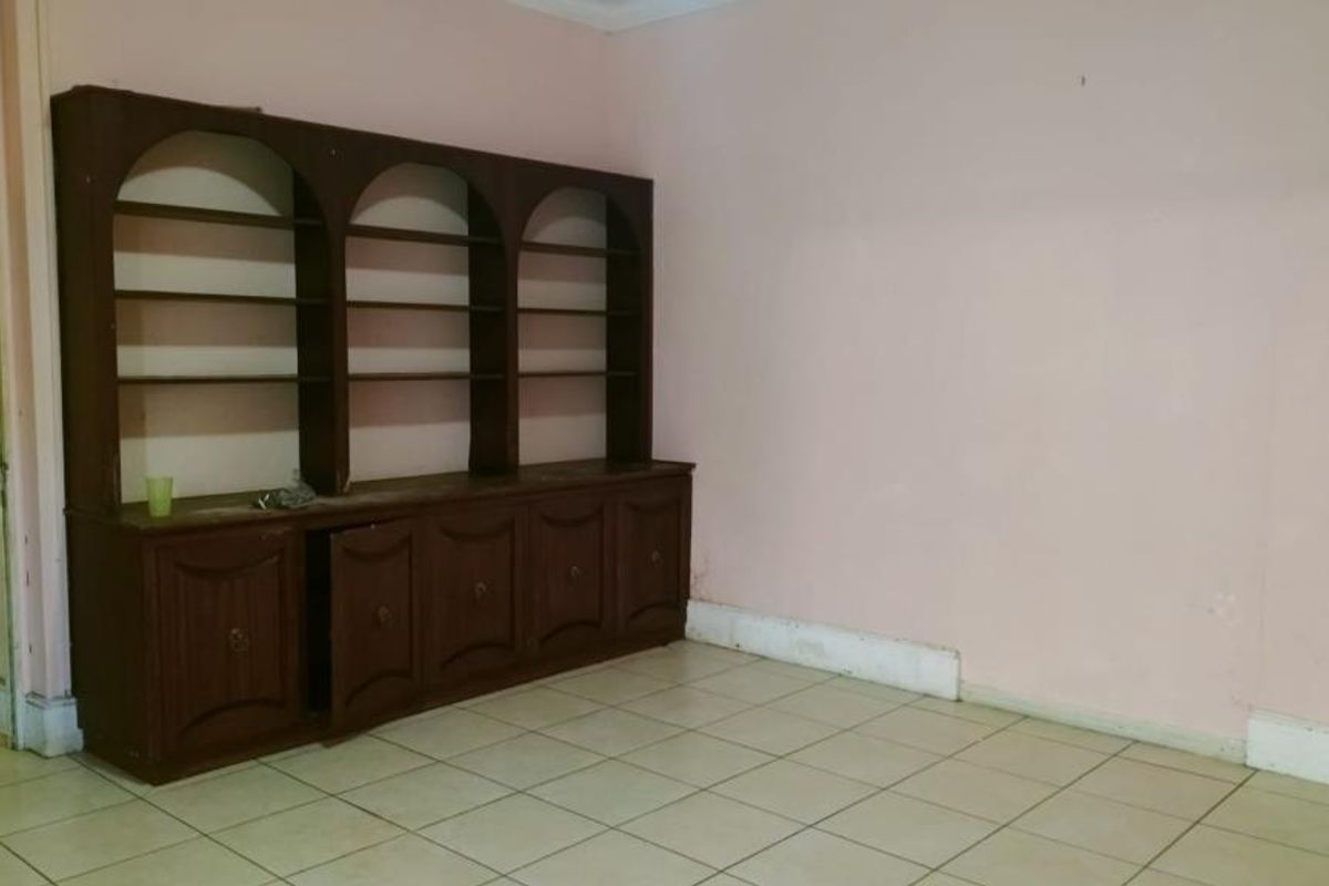 An empty living room featuring ceramic floor tiles and a large, built-in wooden shelving unit with storage cabinetry.