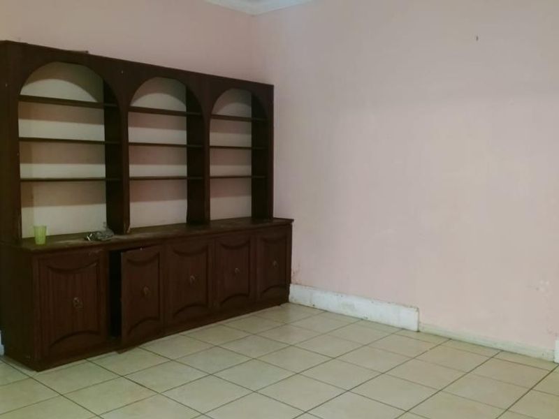 An empty living room featuring ceramic floor tiles and a large, built-in wooden shelving unit with storage cabinetry.