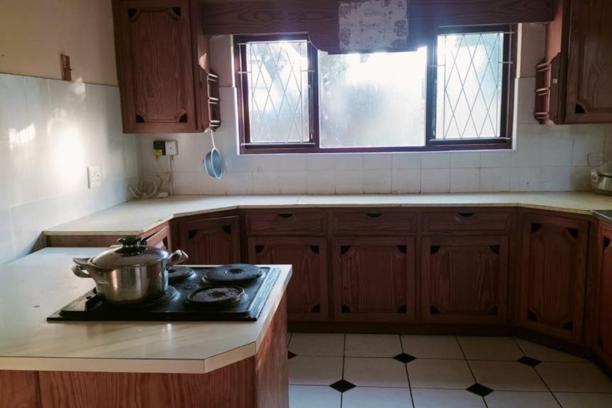 A dated kitchen featuring wooden cabinetry, laminate countertops, an electric hob, and tiled flooring with a classic backsplash.